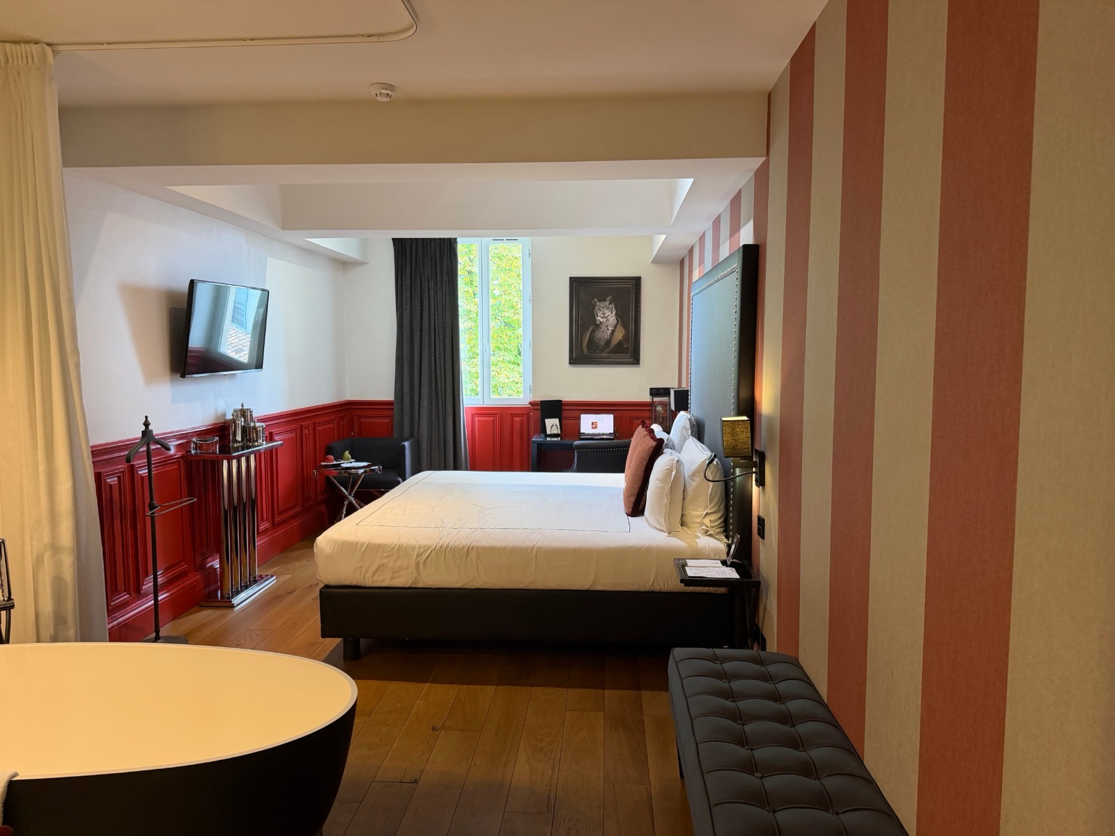 Chambre du Palais Gallien à Bordeaux avec boiseries rouges, lit double, fauteuil, bureau et baignoire en îlot au premier plan