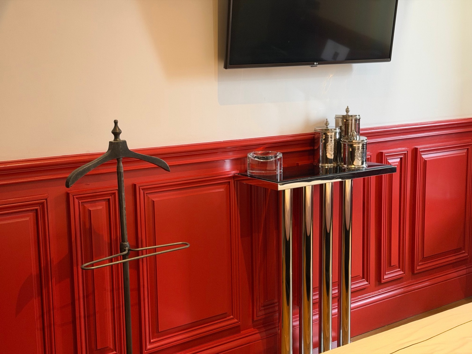 Boiseries rouges, valet de nuit en laiton et console aux pieds en tubes d'acier sous un téléviseur LG dans une chambre du Palais Gallien