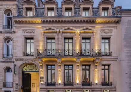 Le Palais Gallien à Bordeaux : notre avis 4,9/5 sur cet hôtel 5 étoiles avec spa Façade éclairée de l'hôtel particulier du Palais Gallien à Bordeaux, avec balcon en fer forgé et porte cintrée