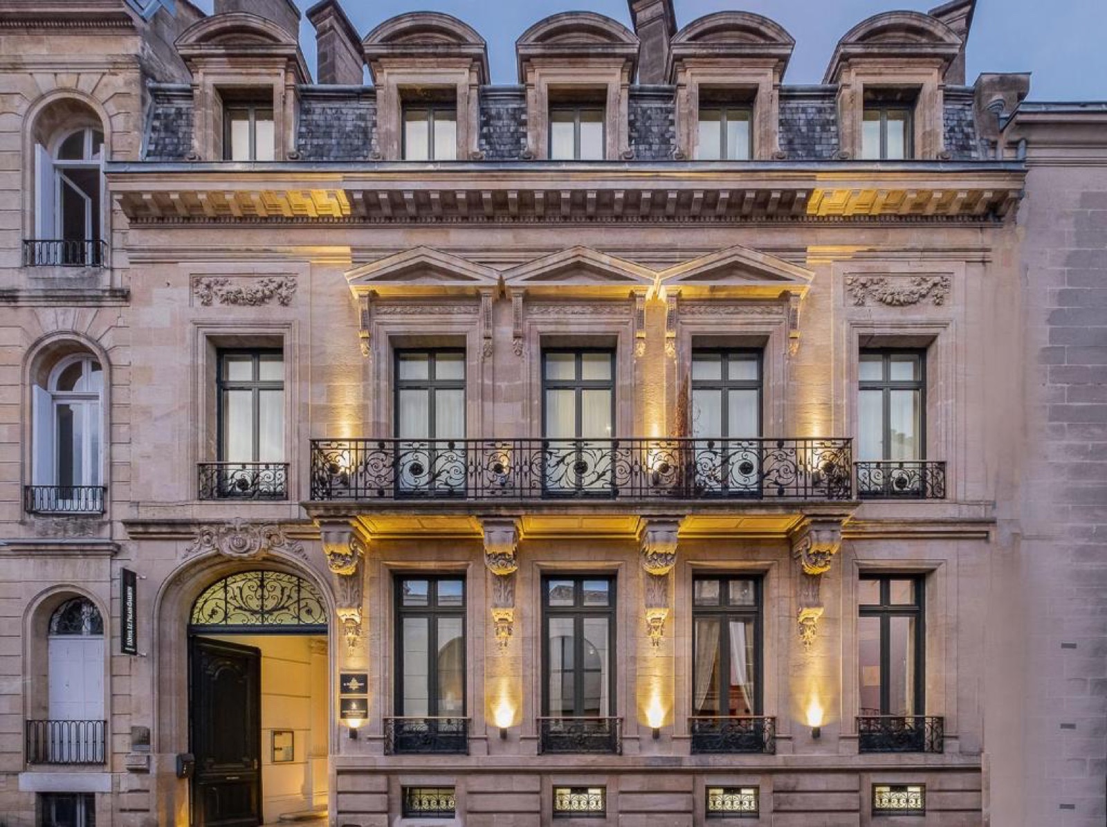 Façade éclairée de l'hôtel particulier du Palais Gallien à Bordeaux, avec balcon en fer forgé et porte cintrée