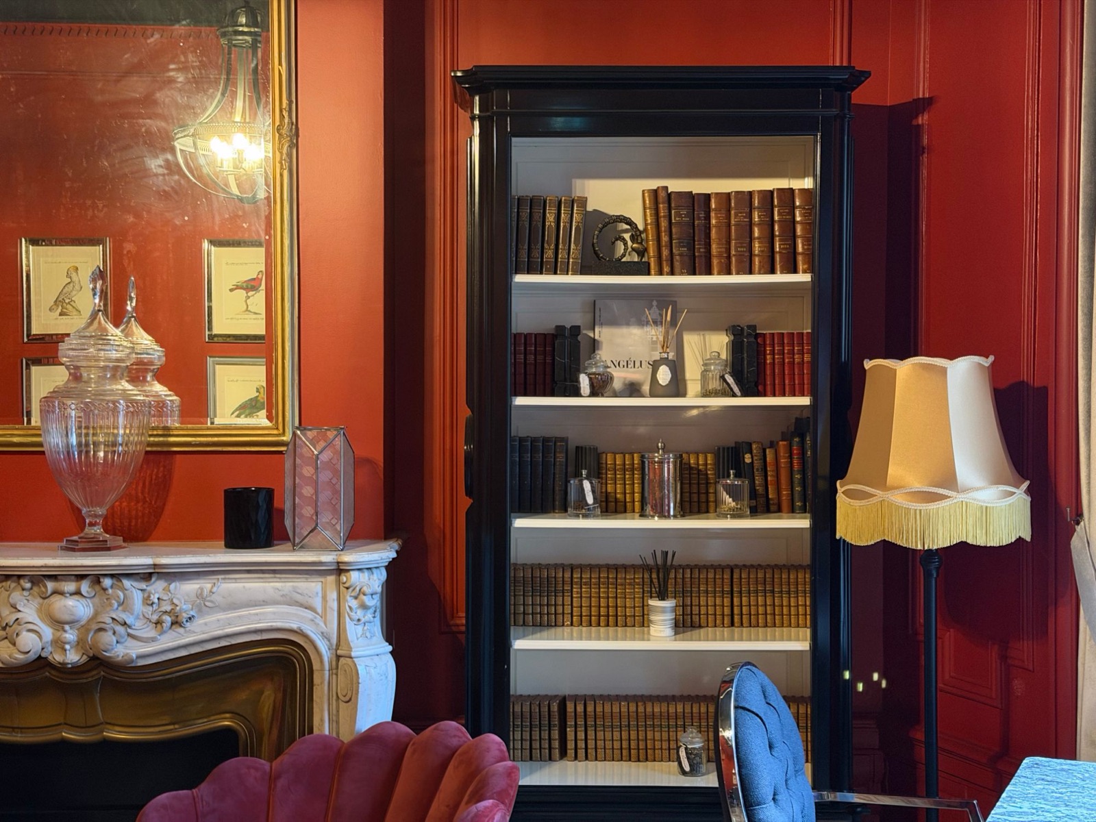 Salon du Palais Gallien avec murs rouges, cheminée en marbre, bibliothèque noire de livres anciens et fauteuil en velours rose